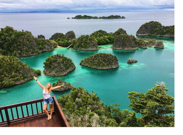 Chloe King waving her arms up in the air, standing in front of Raja Ampat, West Papua.