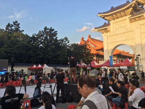 People sitting on stools in front of the Tiananmen Memorial 