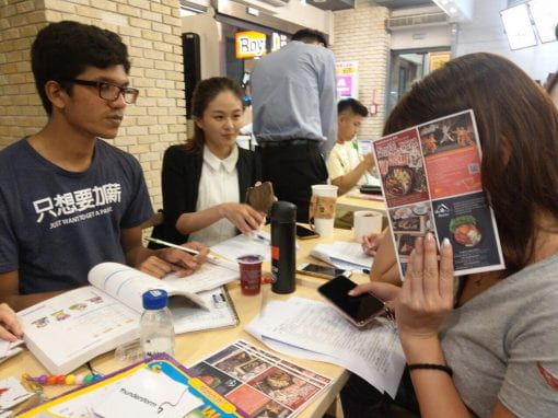 Students working in a group with a female student covering her face with a piece of paper 